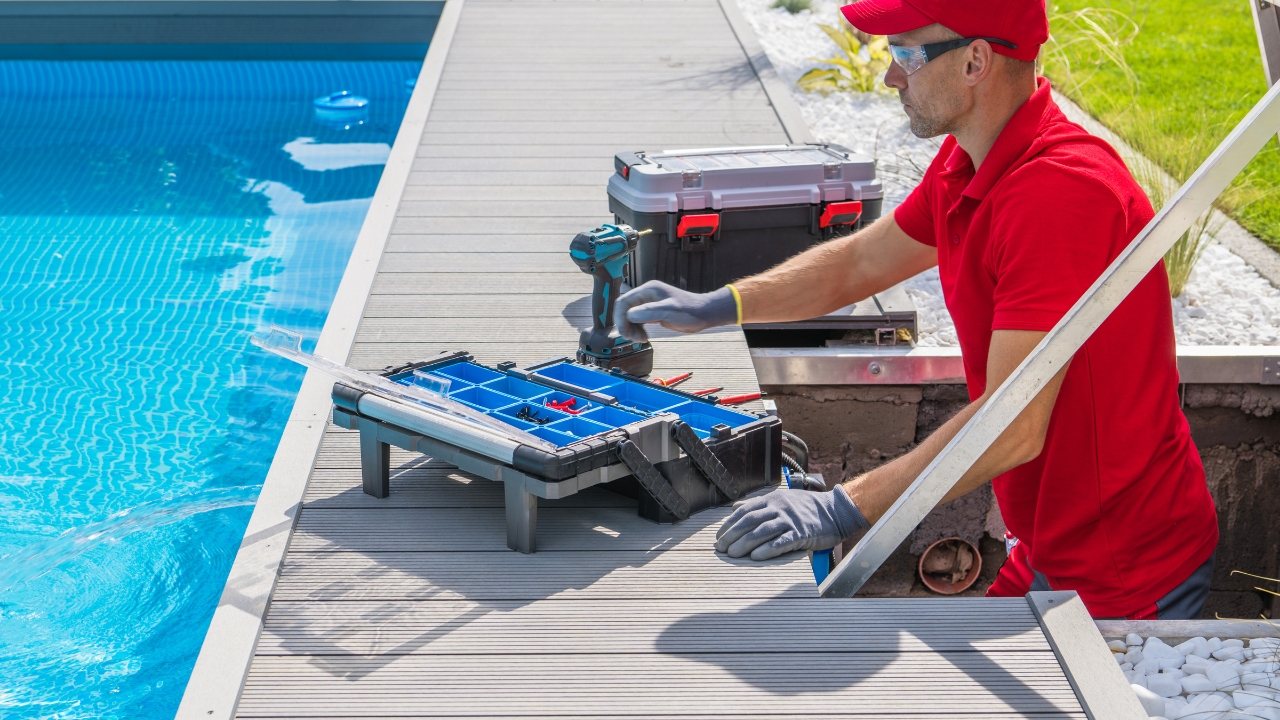 Pool technician in a red shirt and hat, wearing safety gloves and goggles, performing pool repair service